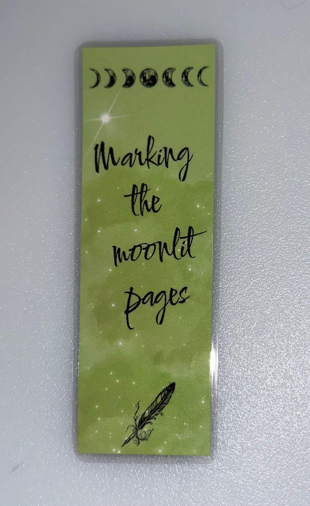 Green bookmark with moon phases and quill illustration- “Marking the Moonlit Pages”