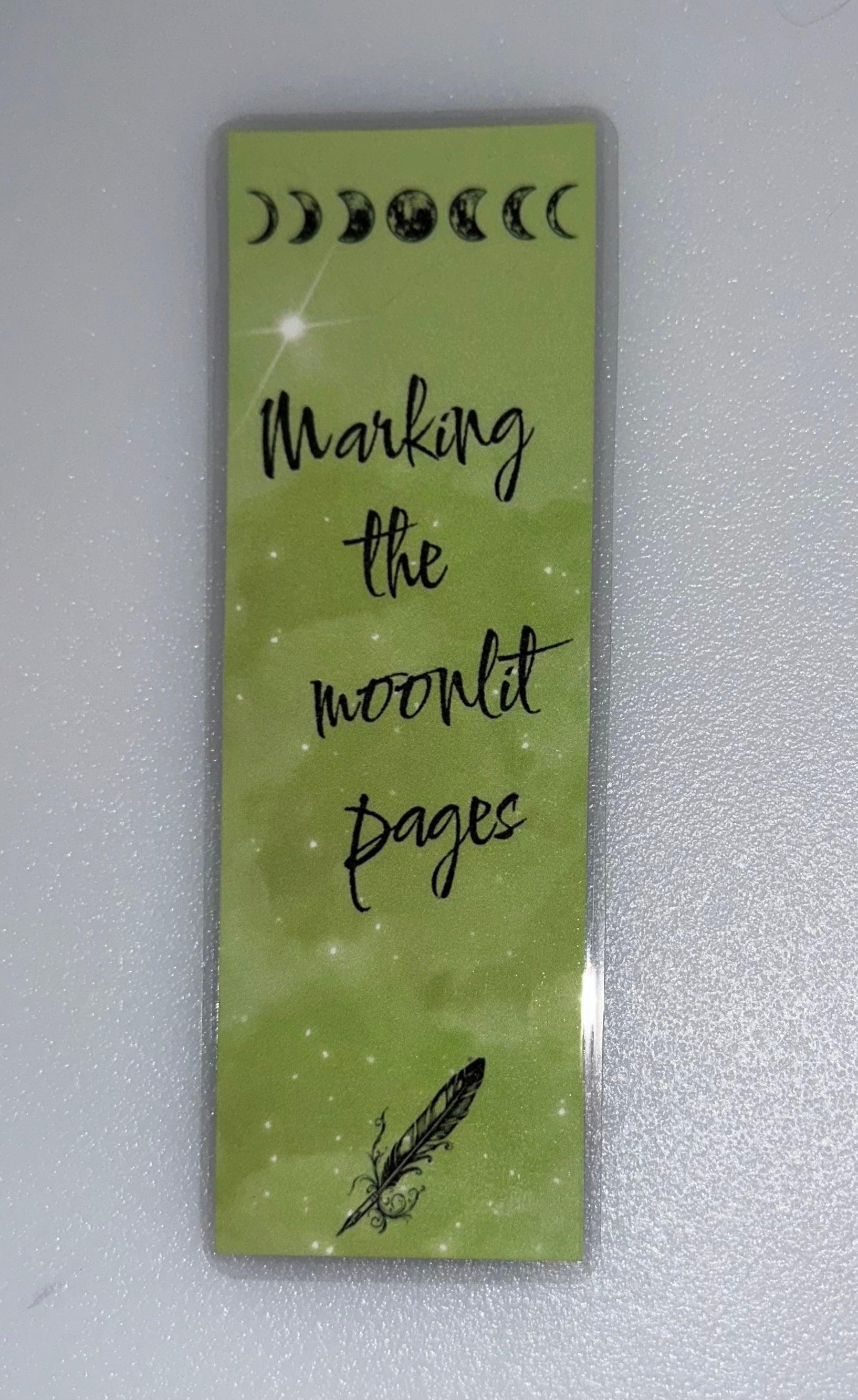 Green bookmark with moon phases and quill illustration- “Marking the Moonlit Pages”